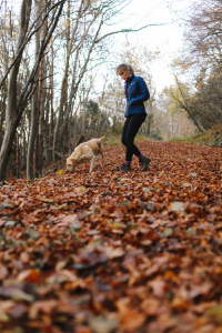 Lady walking her dog in open grounds with trees 
